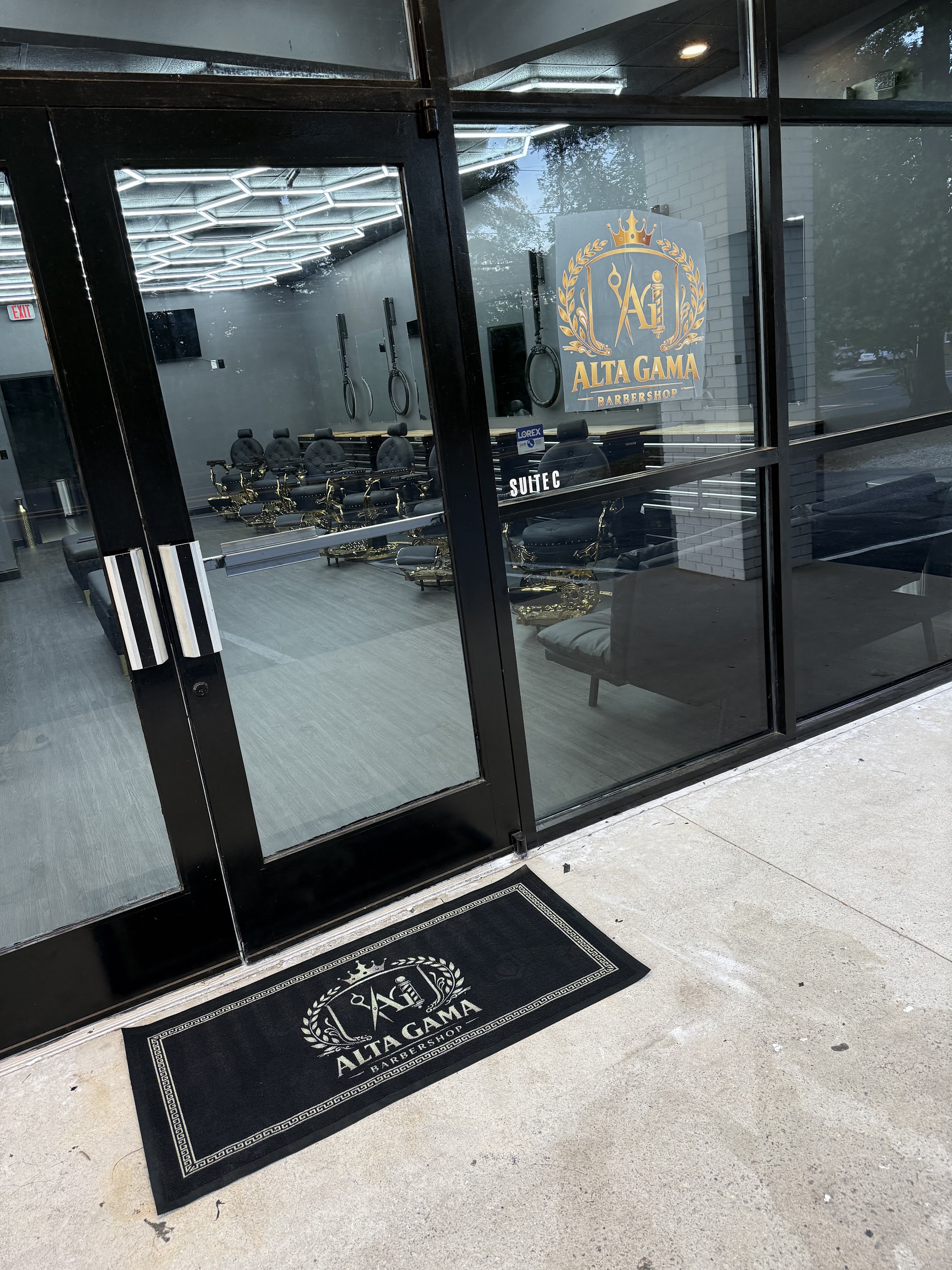 The front door of Alta Gama Barbershop with the gold crest on the glass and doormat